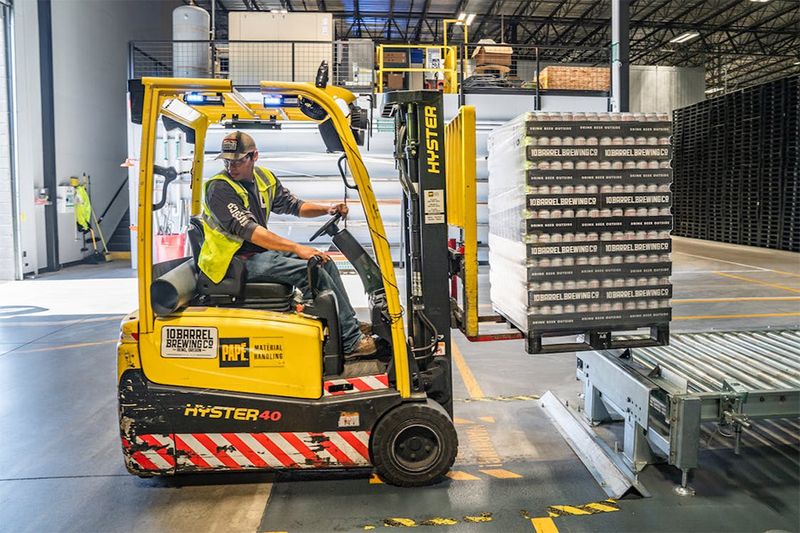 A photo of a man driving a forklift in a high-vis jacket.