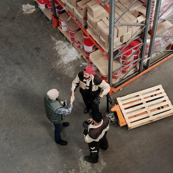 A photo of a birdseye view of three people in a warehouse, two of them are shaking hands.