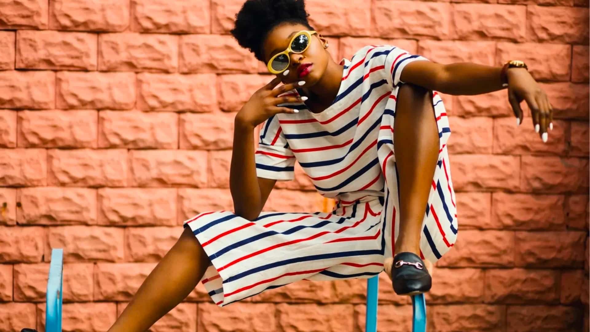 A photo of a model posing with a striped outfit on and sunglasses.