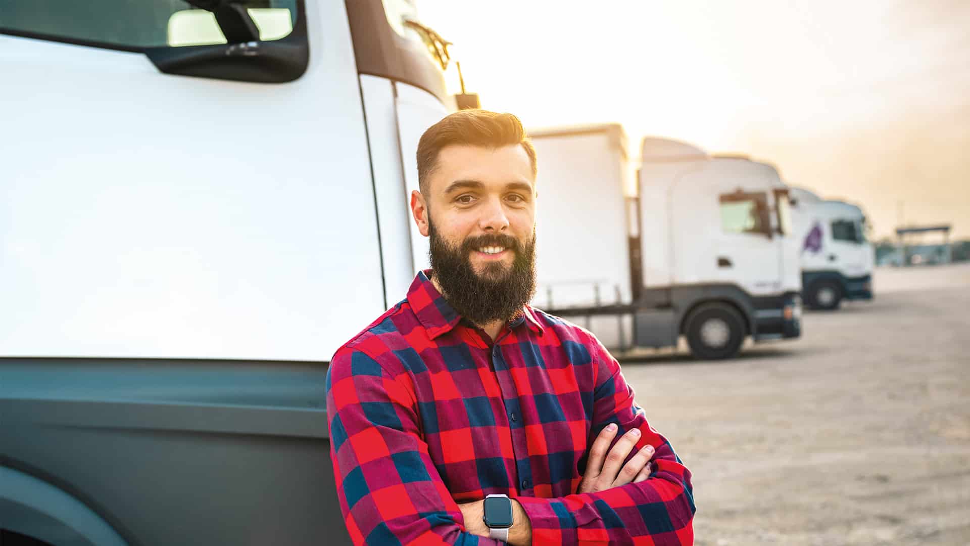 A photo of a man with a beard stood in front of trucks.
