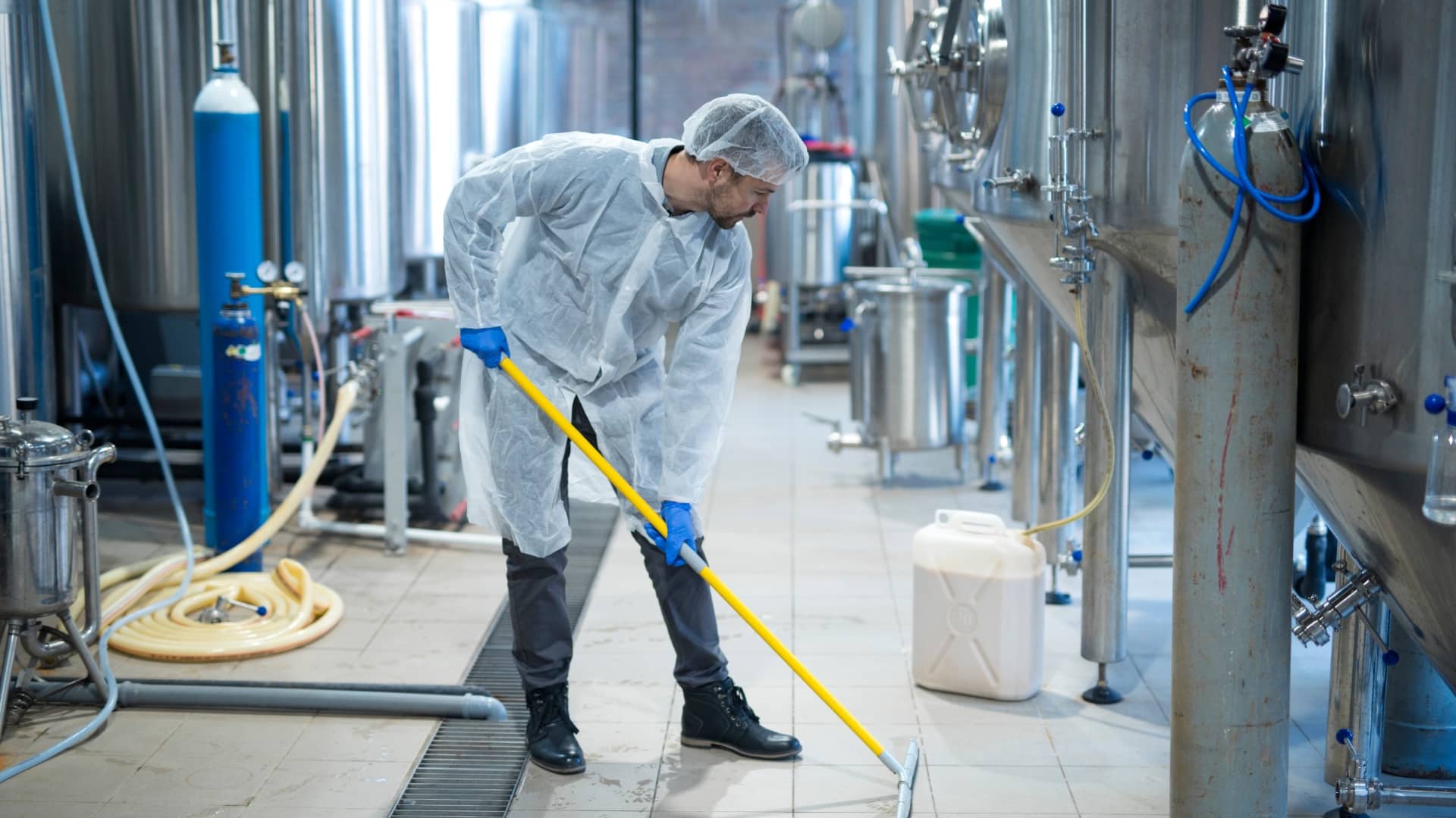 A photo of a man in protective gear, cleaning at a factory.