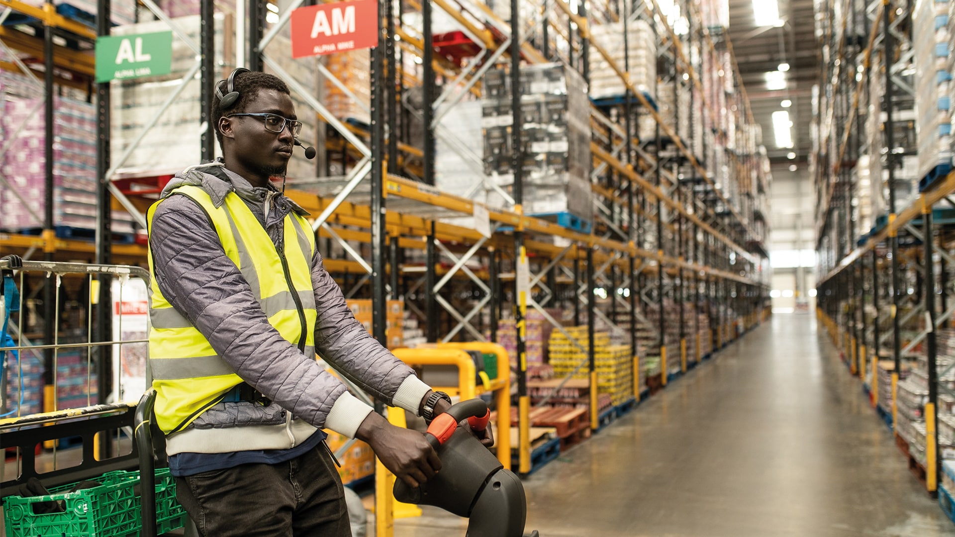 A photo of a man with a headset on and a high-vis at a warehouse.
